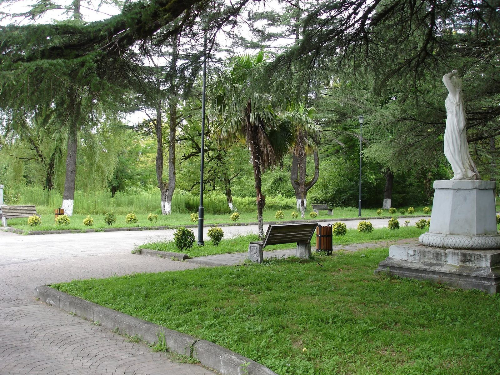 Der Stadtpark: Blumenbeete, Bänke und eine Marmorstatue am Weg.