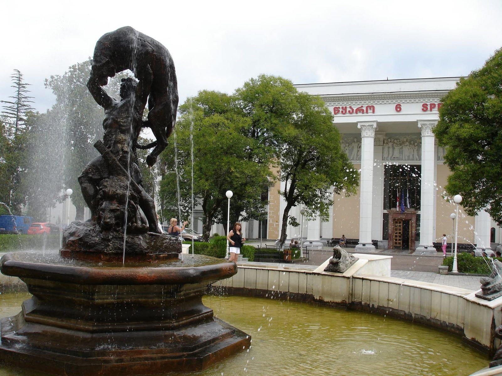 Ein Brunnen mit Skulptur vor einem Gebäude mit Säulen.