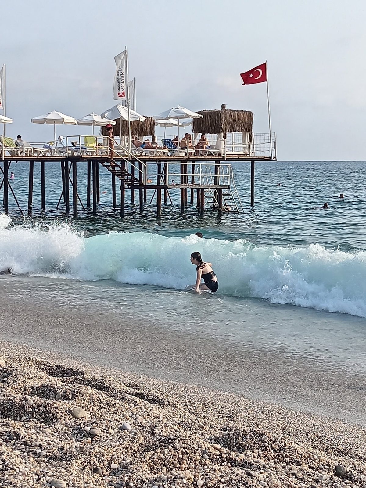 Ein Strand mit Wellen und einem hölzernen Steg. Am Mast weht eine Flagge.